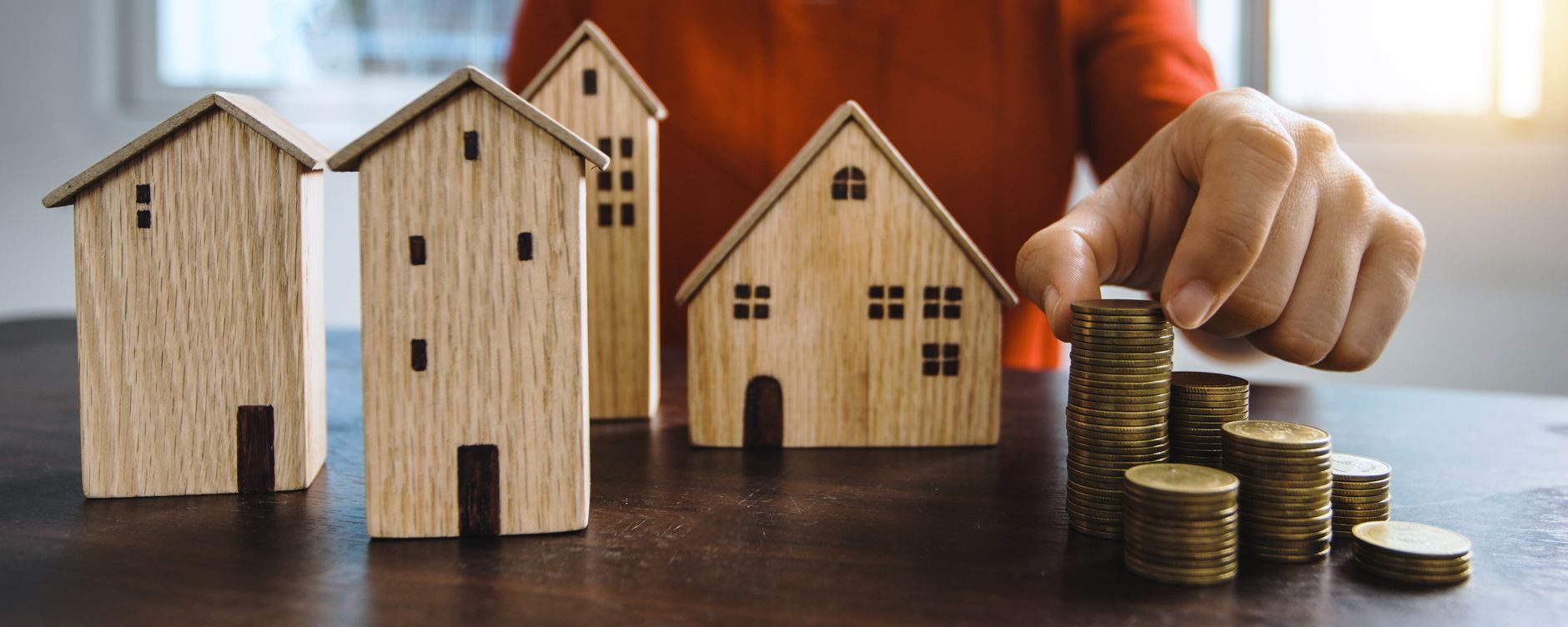 Model wooden houses lined up beside a hand stacking coins, representing growing home equity
